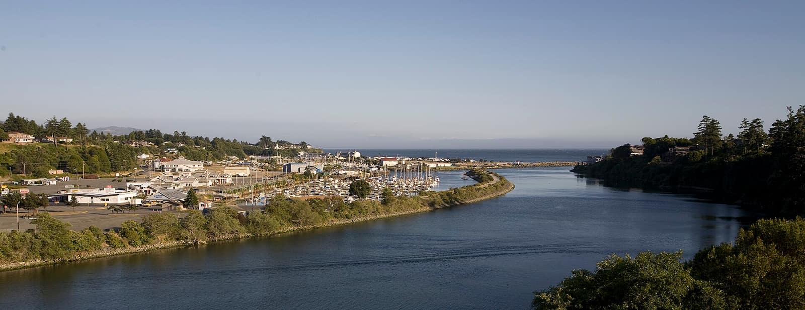 The mouth of the Chetco River and the Brookings harbor, with moored boats and wooded hillsides on both banks