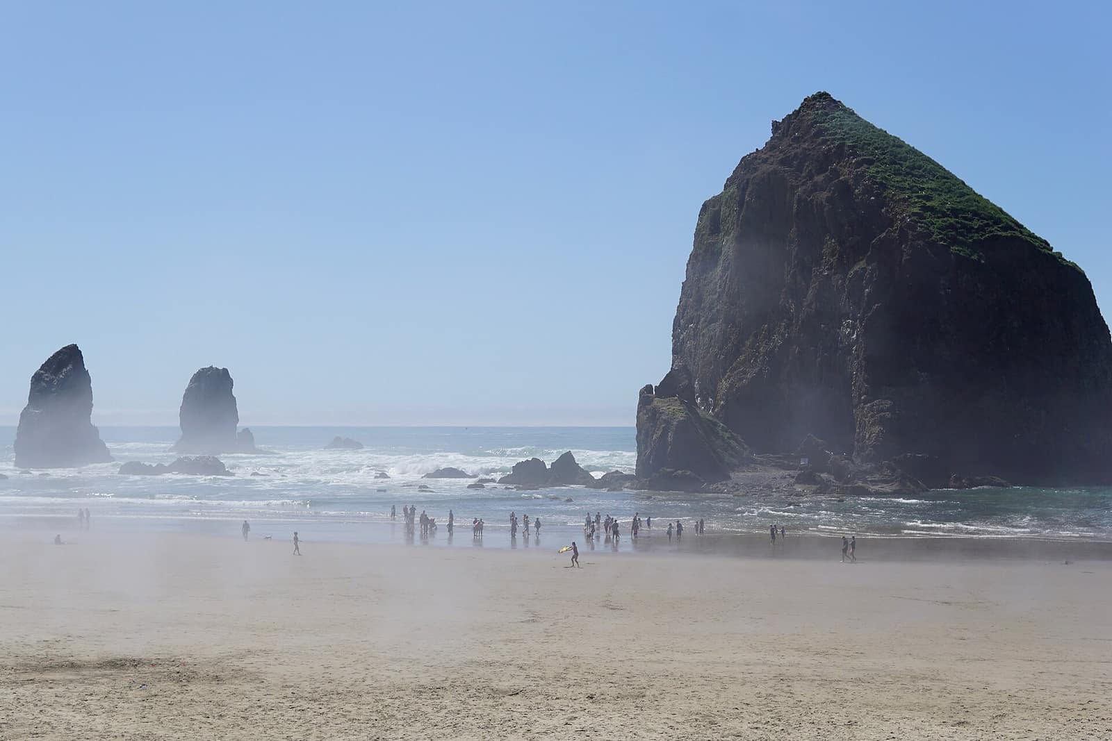 Haystack Rock and the Needles rising from the beach at Cannon Beach with visitors near the surf