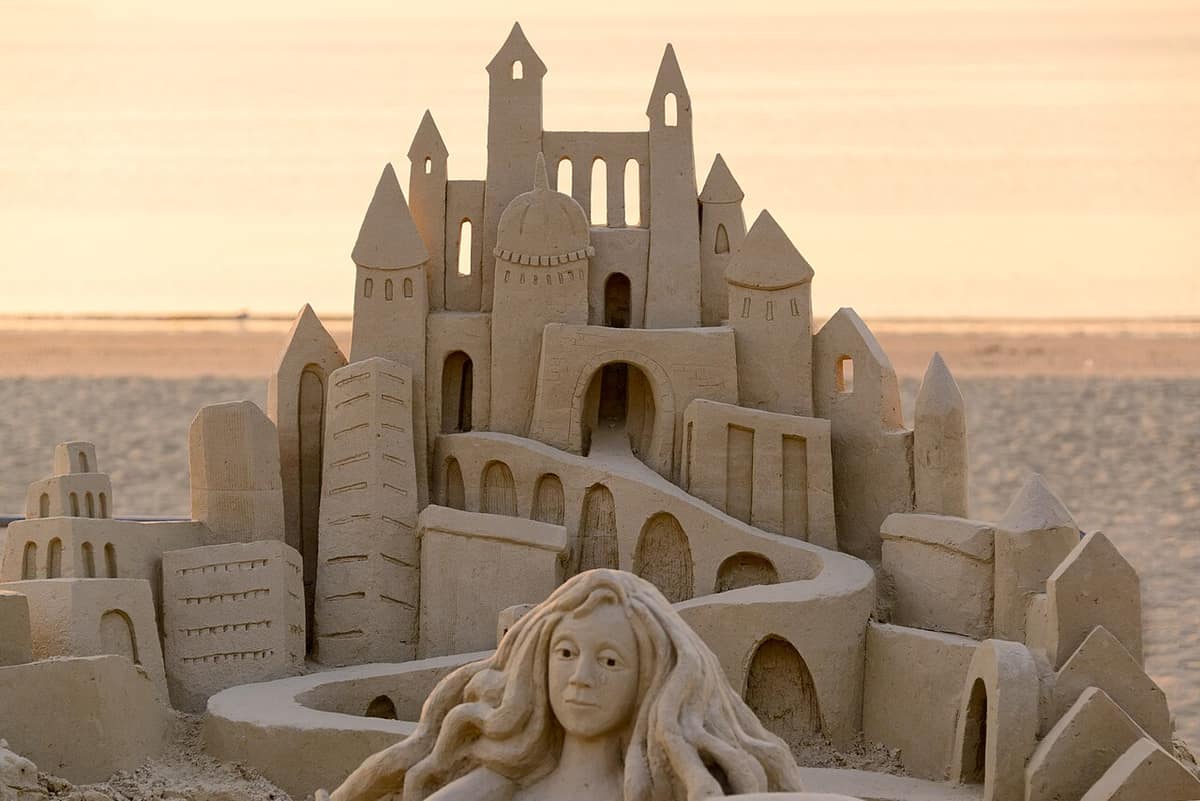 detailed sand castle sculpture with a carved face on a beach