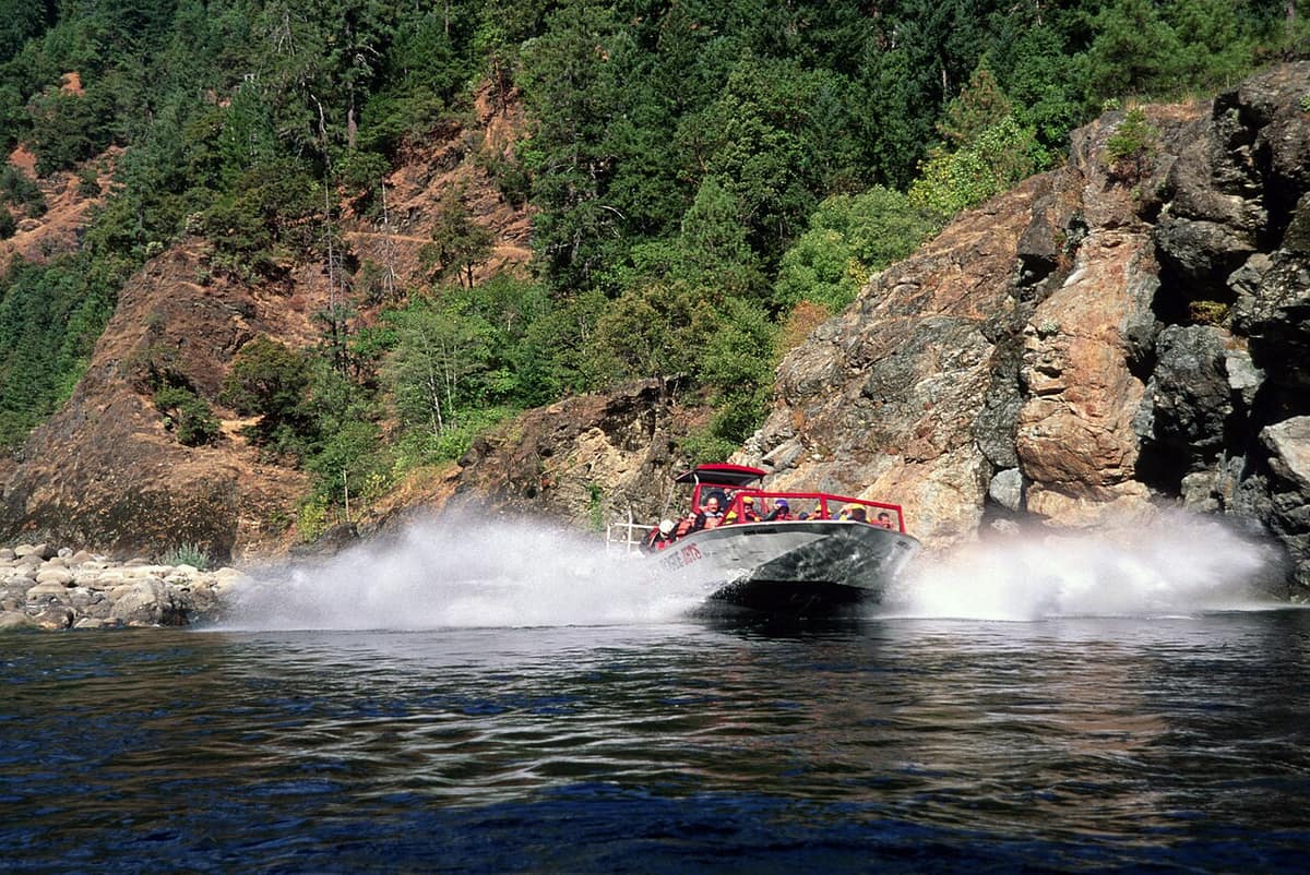 jet boat throwing spray beside rocky canyon walls on the Rogue River
